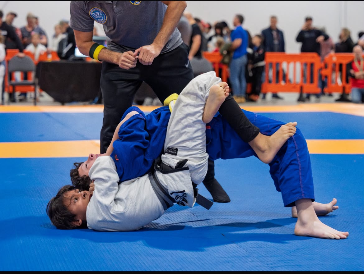 Two youth Jiu Jitsu competitors grappling during a supervised tournament match